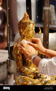 person applying gold leaf offerings to a buddha statue wat phra kaew B8BF5P